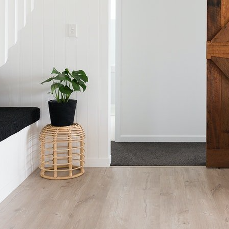 A potted plant is sitting on a wicker stool in a hallway.