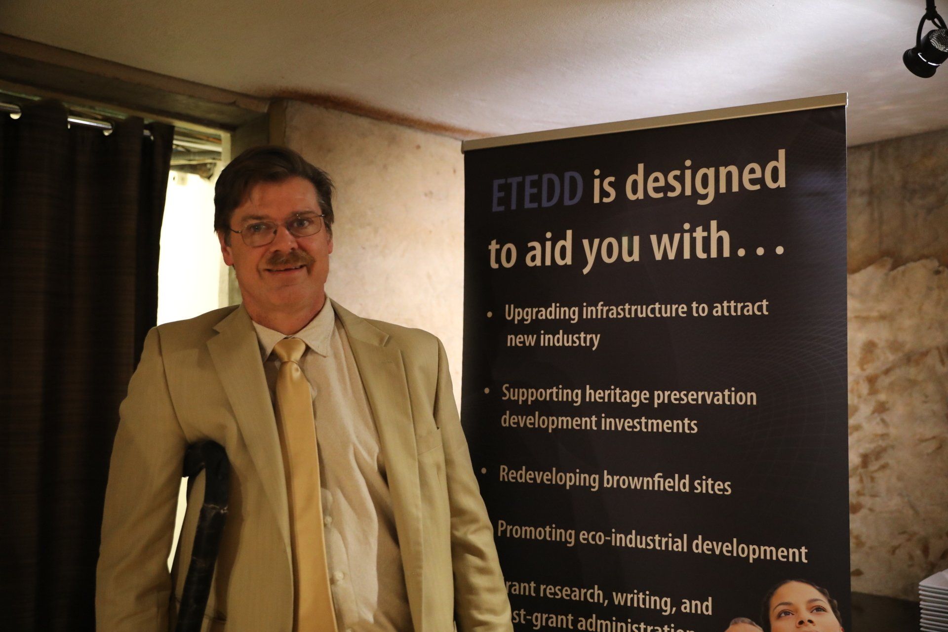 A man with crutches stands in front of a sign that says etedd is designed to aid you with