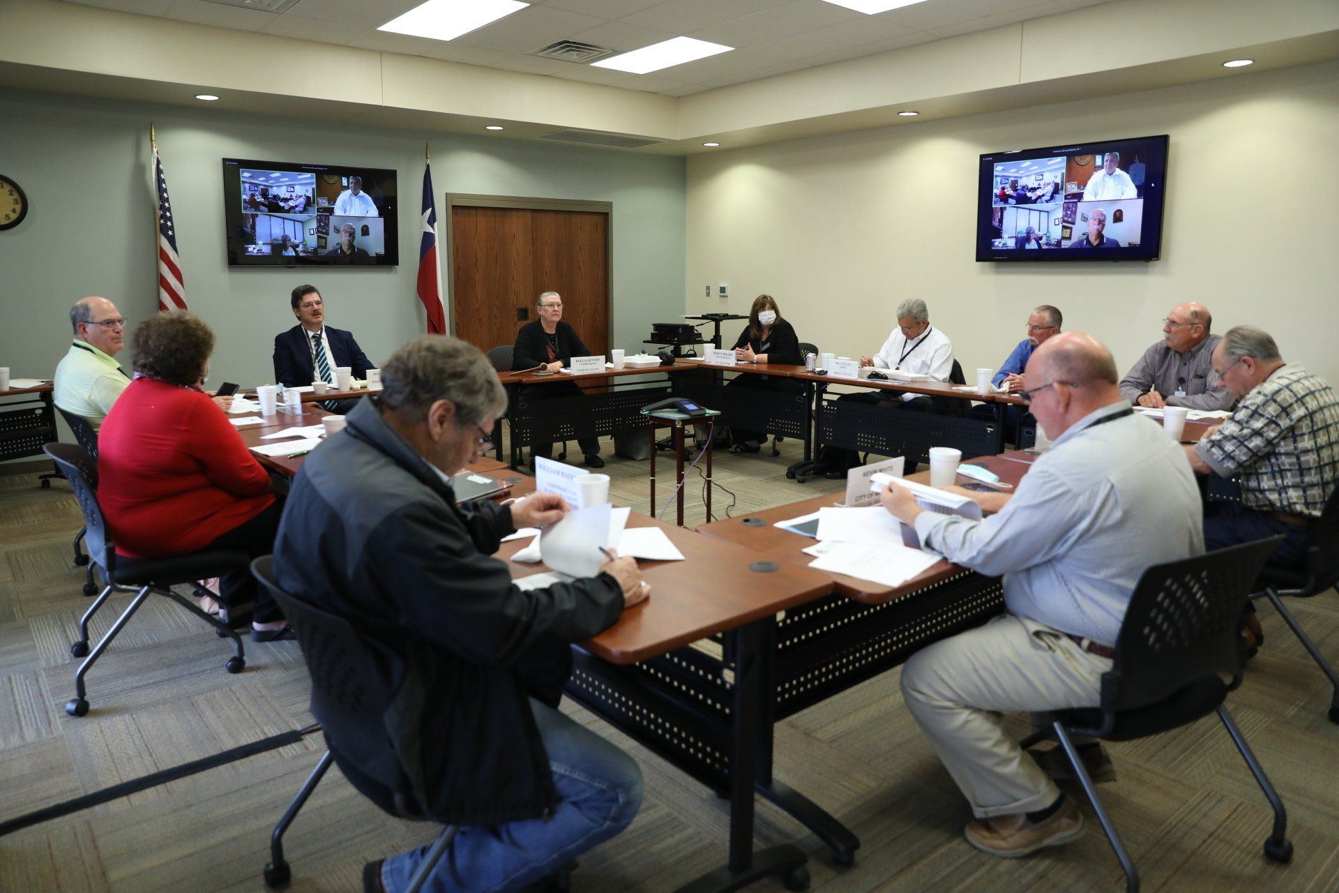 People seated around a conference table in a meeting room, reviewing papers with screens at the front.