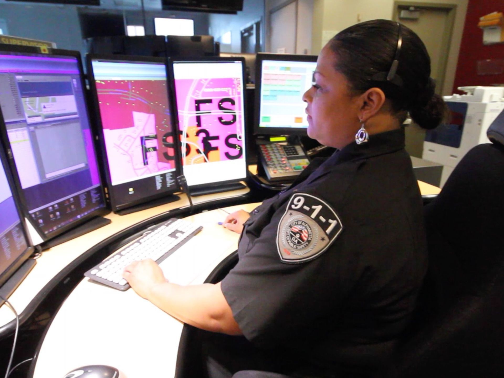 A woman wearing a 9-1-1 patch sits at a desk