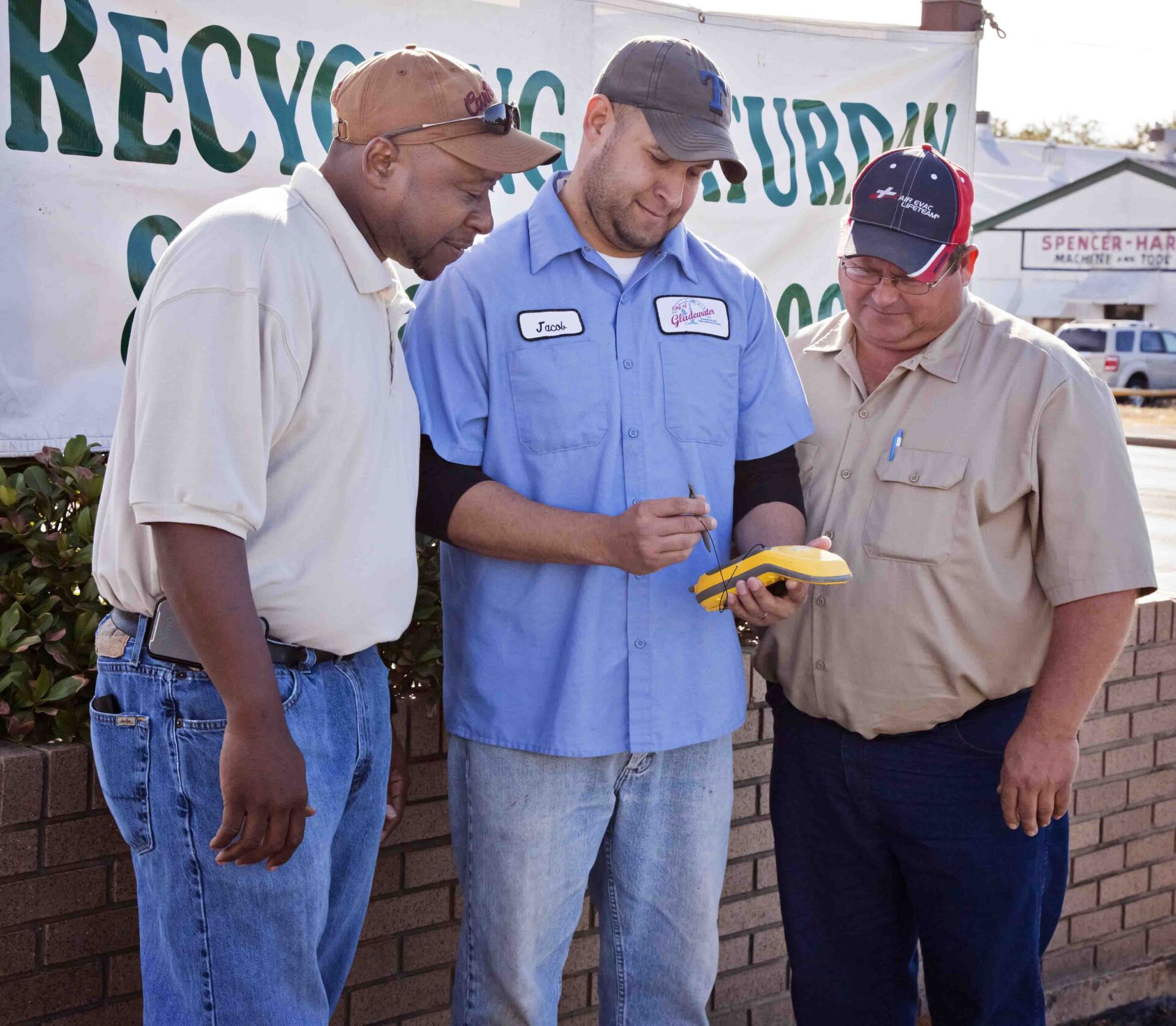 Three men are standing in front of a sign that says recycling