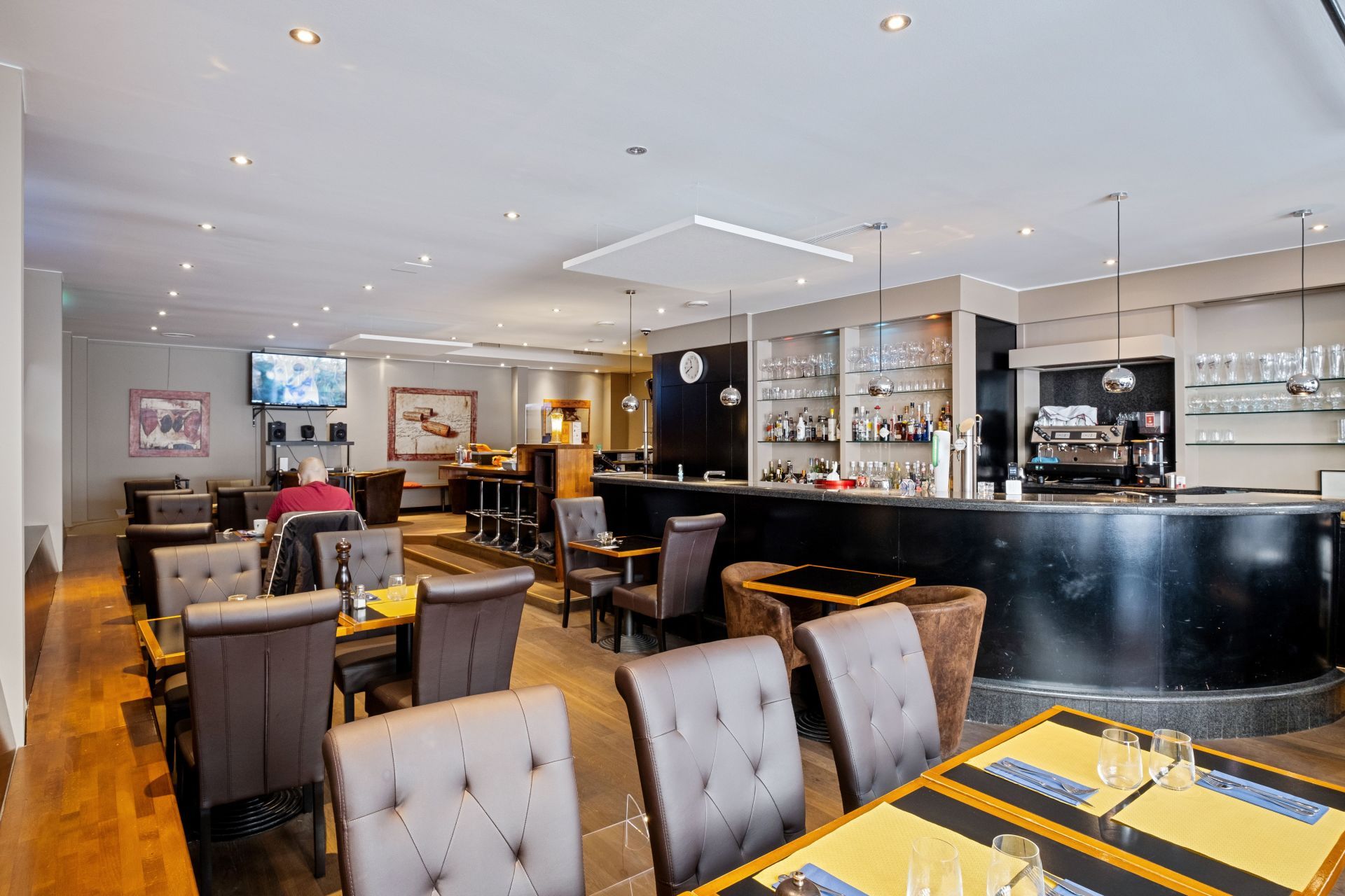 Moderne Hotellounge mit gepolsterten Sesseln, Esstischen und einer geschwungenen schwarzen Bar unter sanfter Beleuchtung