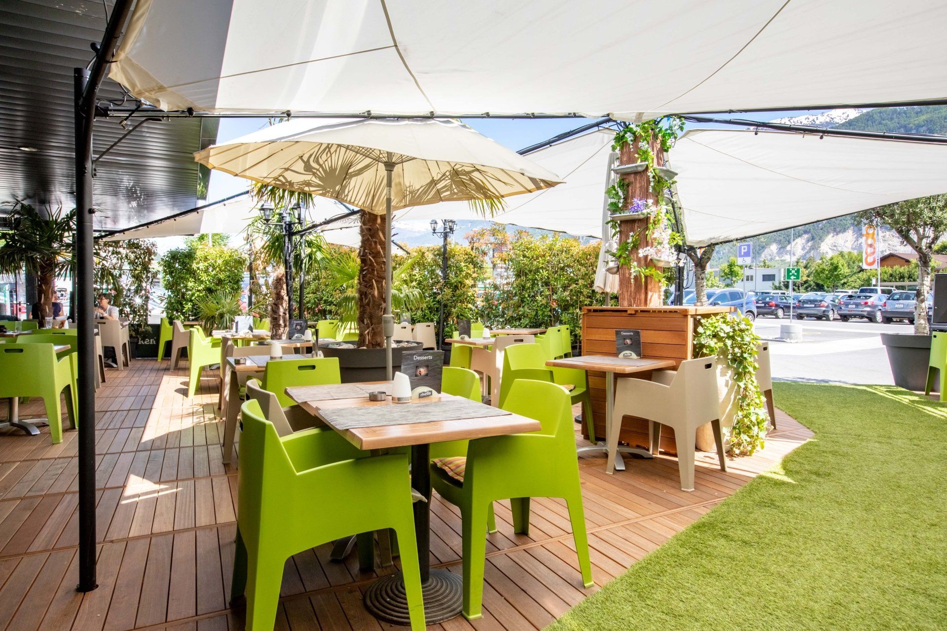 Sitzgelegenheiten im Freien mit limettengrünen Stühlen, Holztischen, Sonnenschirmen und einer sonnigen Terrasse an der Straße