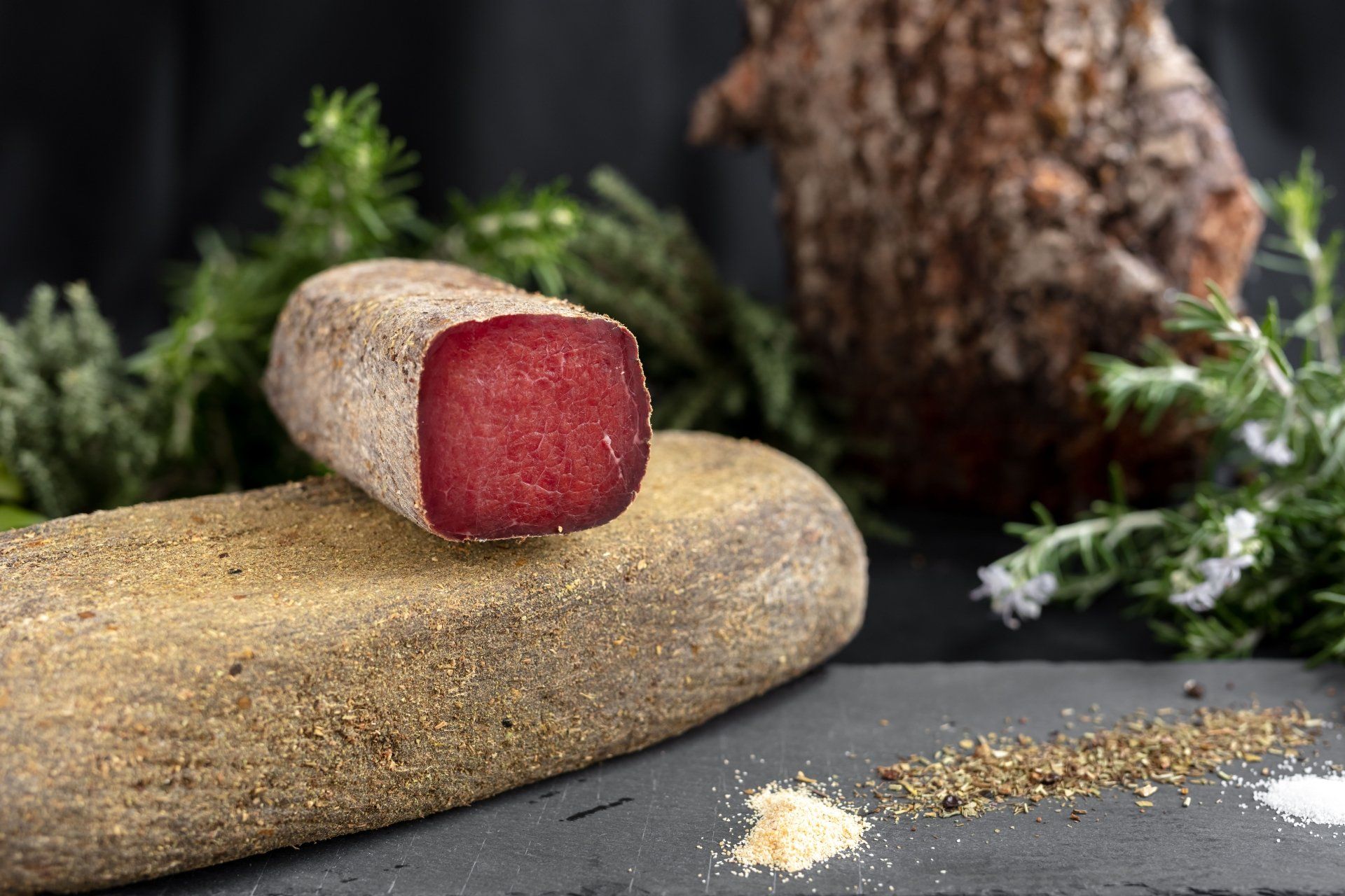 Ein Laib gepökeltes Fleisch auf Brot mit Gewürzen und Kräutern auf dunkler Oberfläche