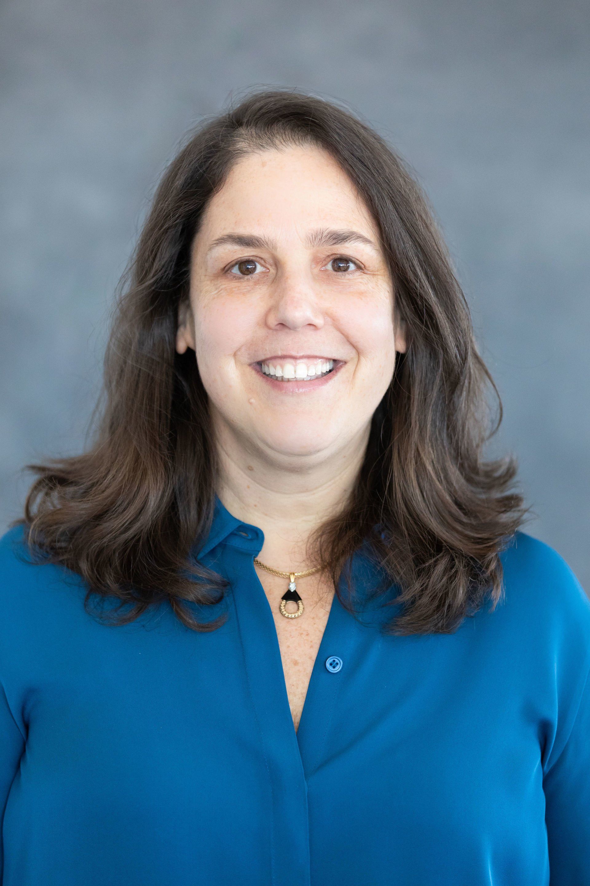 A woman in a blue shirt is smiling for the camera.