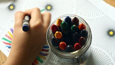 A child is drawing with a crayon next to a jar of crayons.
