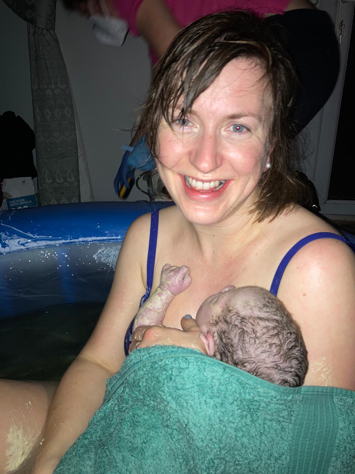 A woman is holding a newborn baby in her arms and smiling.