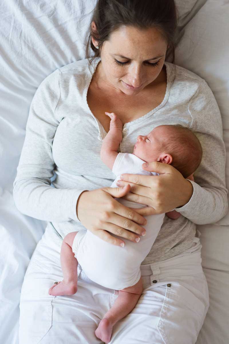 A woman is holding a newborn baby in her arms while laying on a bed.