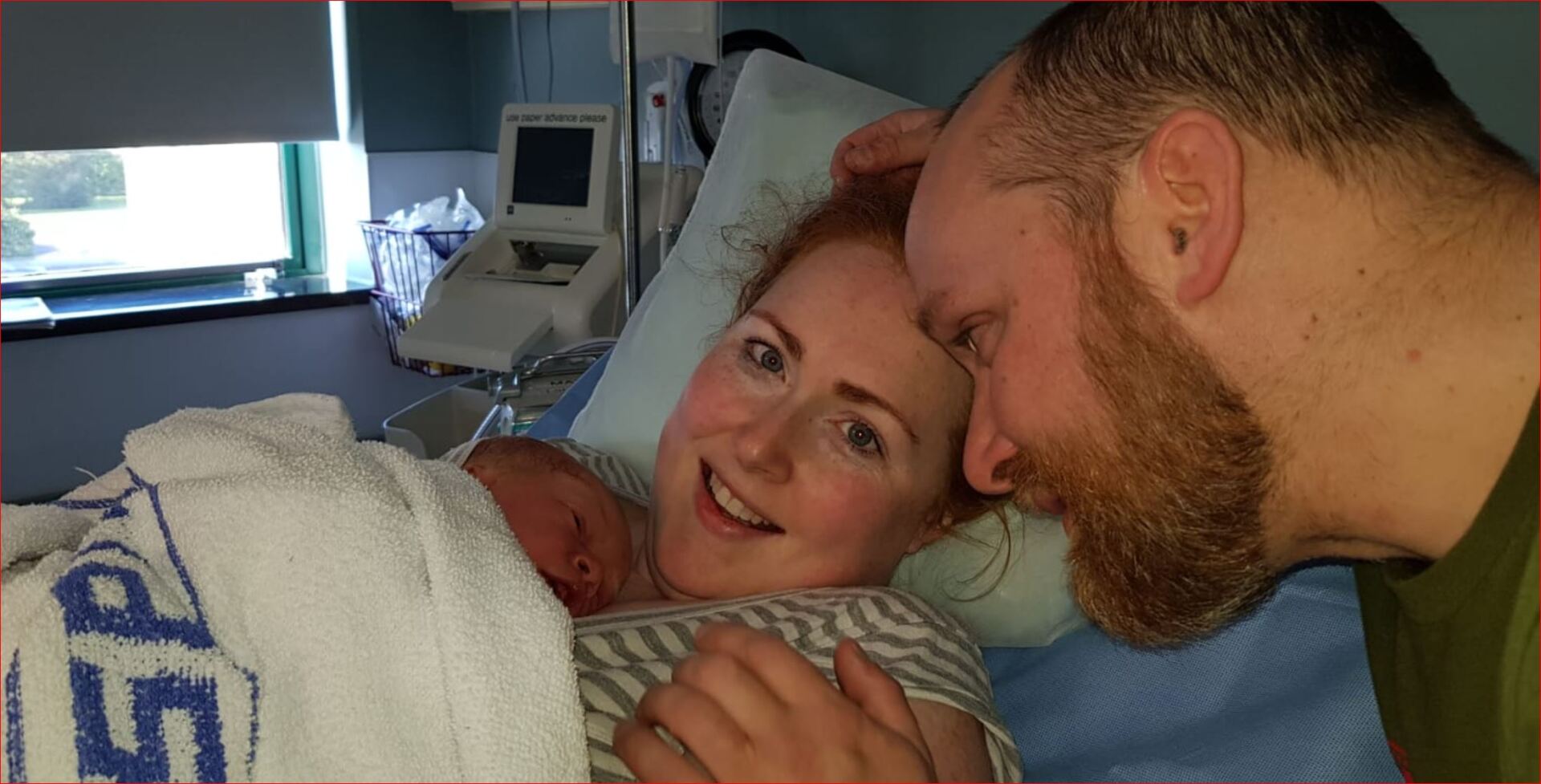 A man and woman are holding a newborn baby in a hospital bed.