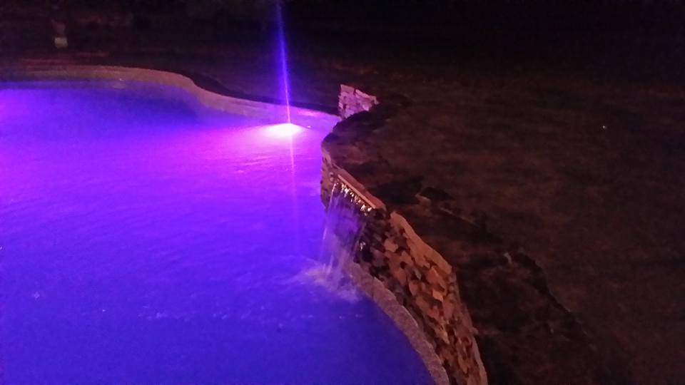 A swimming pool with purple lights on it at night.