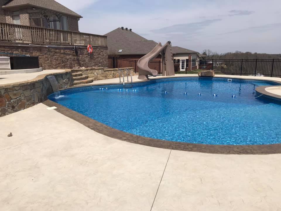 A large swimming pool with a slide in the backyard of a house.