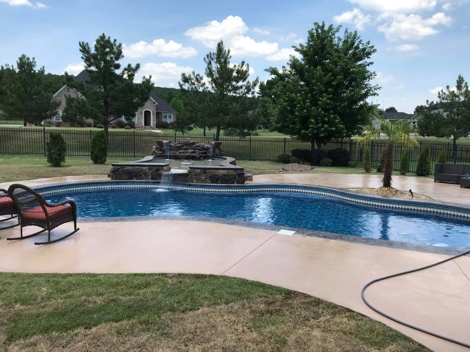 A large swimming pool in a backyard with rocking chairs and a hose.