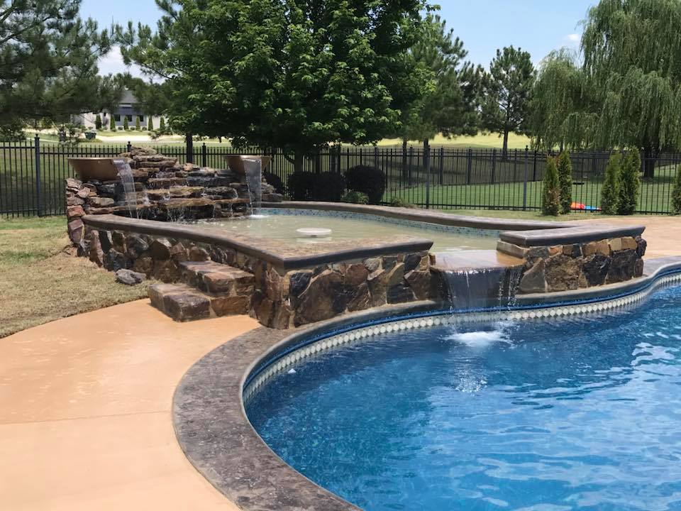 A large swimming pool with a waterfall in the backyard.