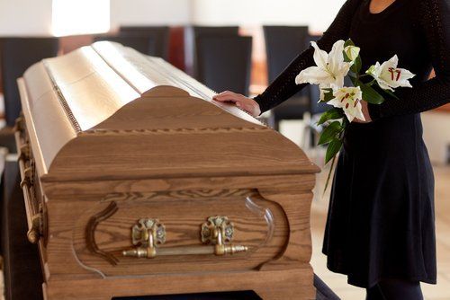 donna vestita di nero che accarezza una bara con dei fiori in mano