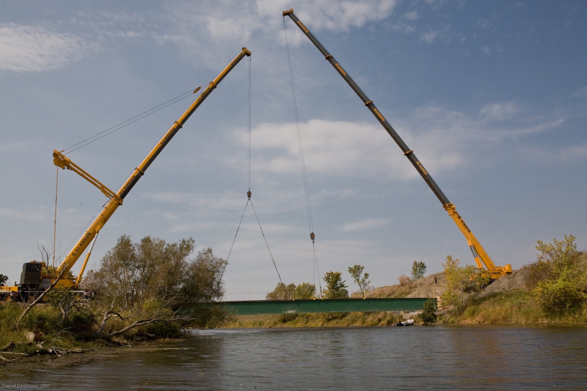 Two cranes are lifting a bridge over a body of water