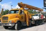 A yellow truck with a crane on top of it is parked in a parking lot.