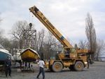 A large yellow crane is lifting a boat in a parking lot.