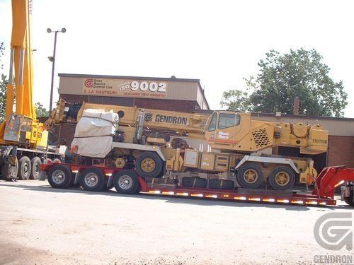 A large yellow crane is on a trailer in front of a building that says 9002