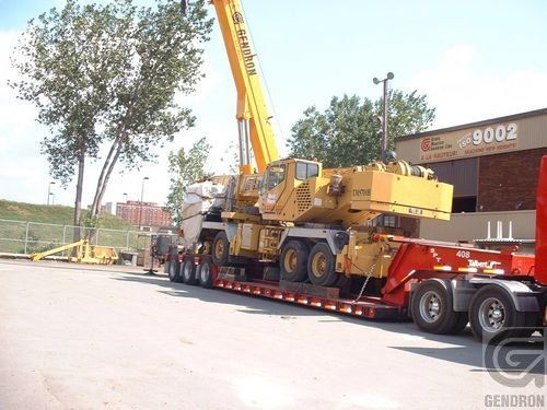 A truck with a crane on the back is parked in front of a building that says 9002
