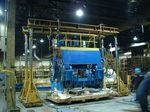 A large blue machine is sitting on top of a wooden pallet in a factory.