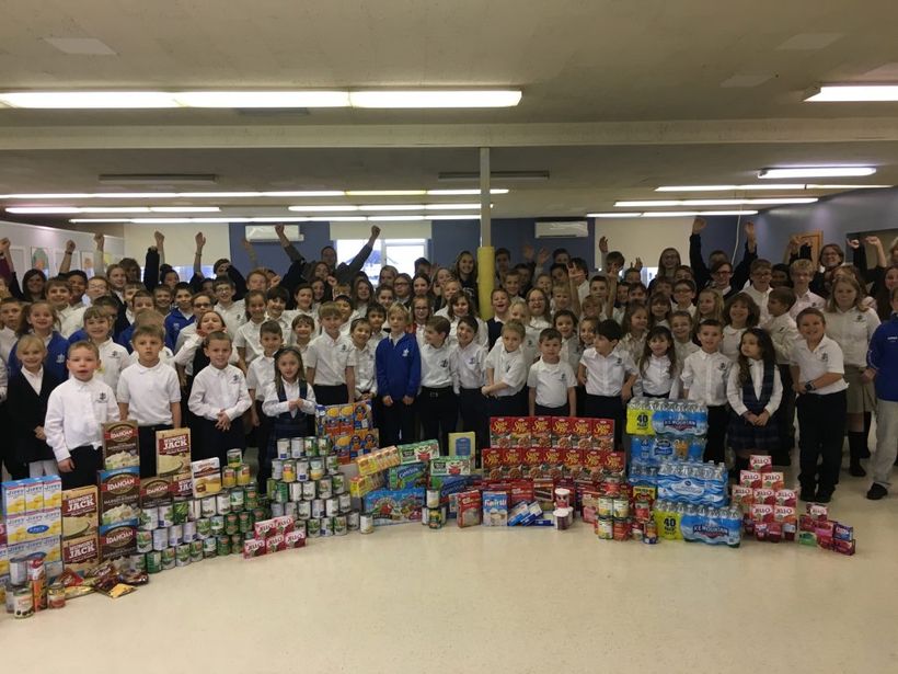 A large group of children are posing for a picture in front of a pile of food