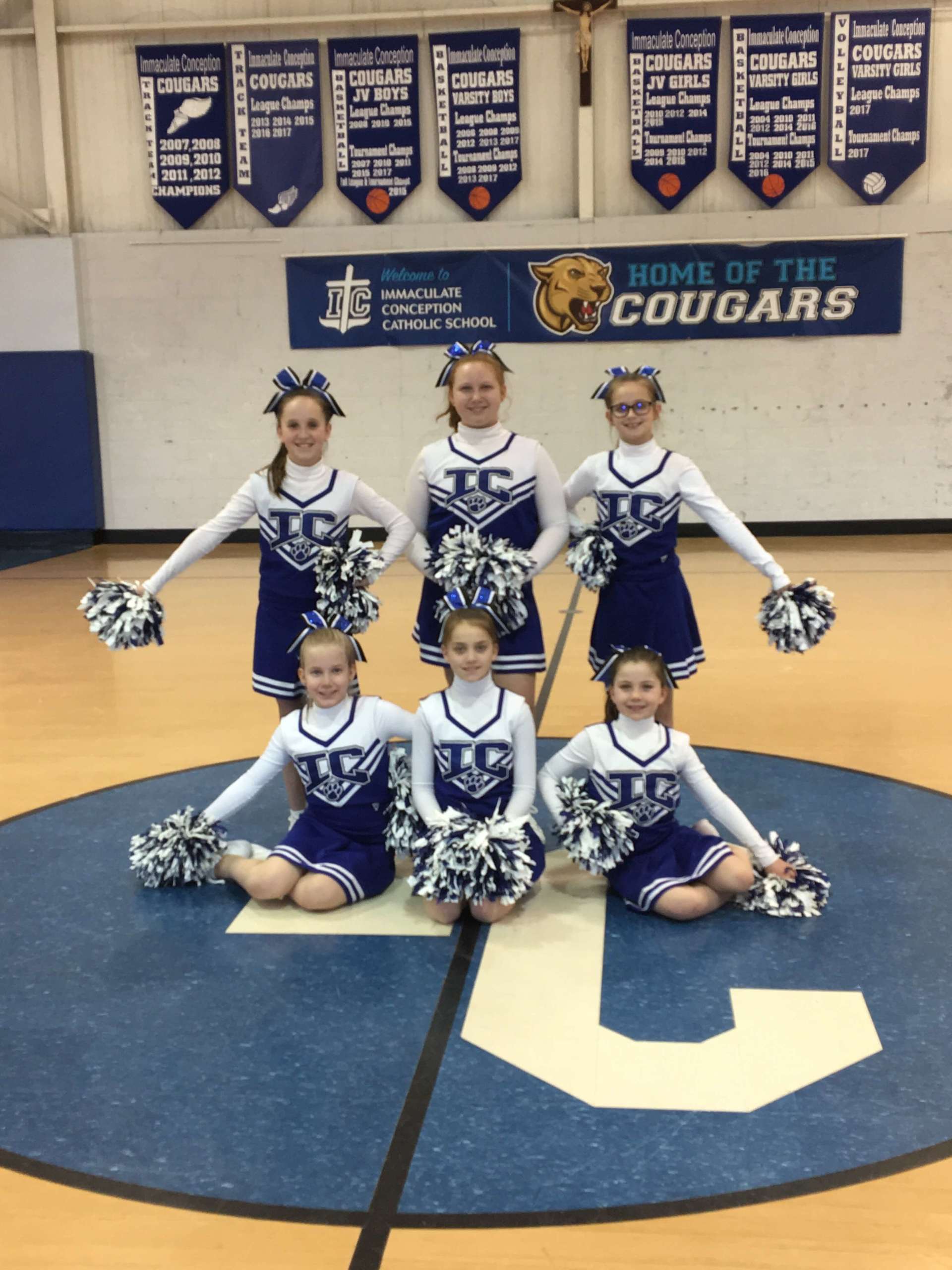 Cheerleaders pose in front of a sign that says home of the cougars