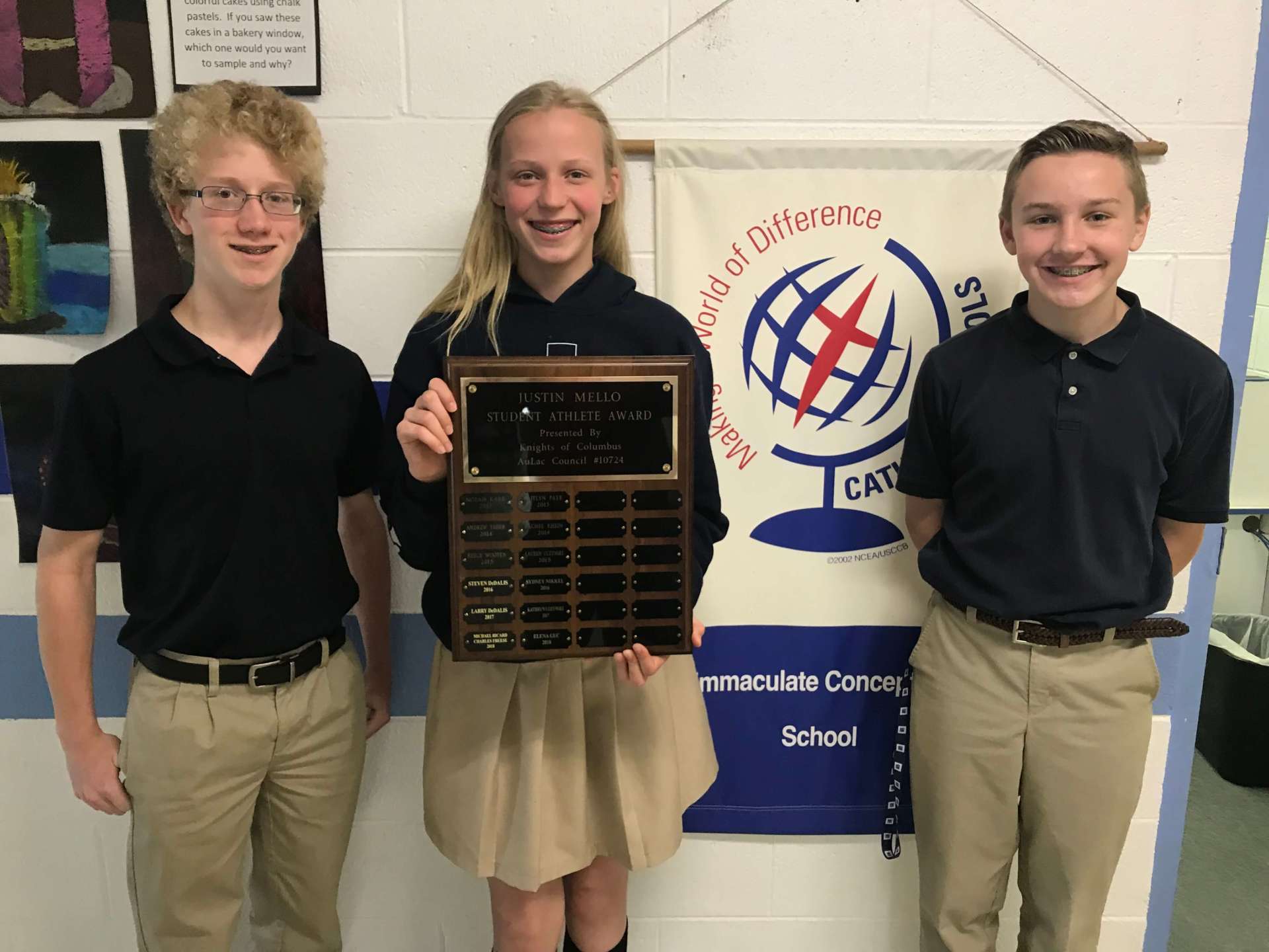 Three students holding a plaque.