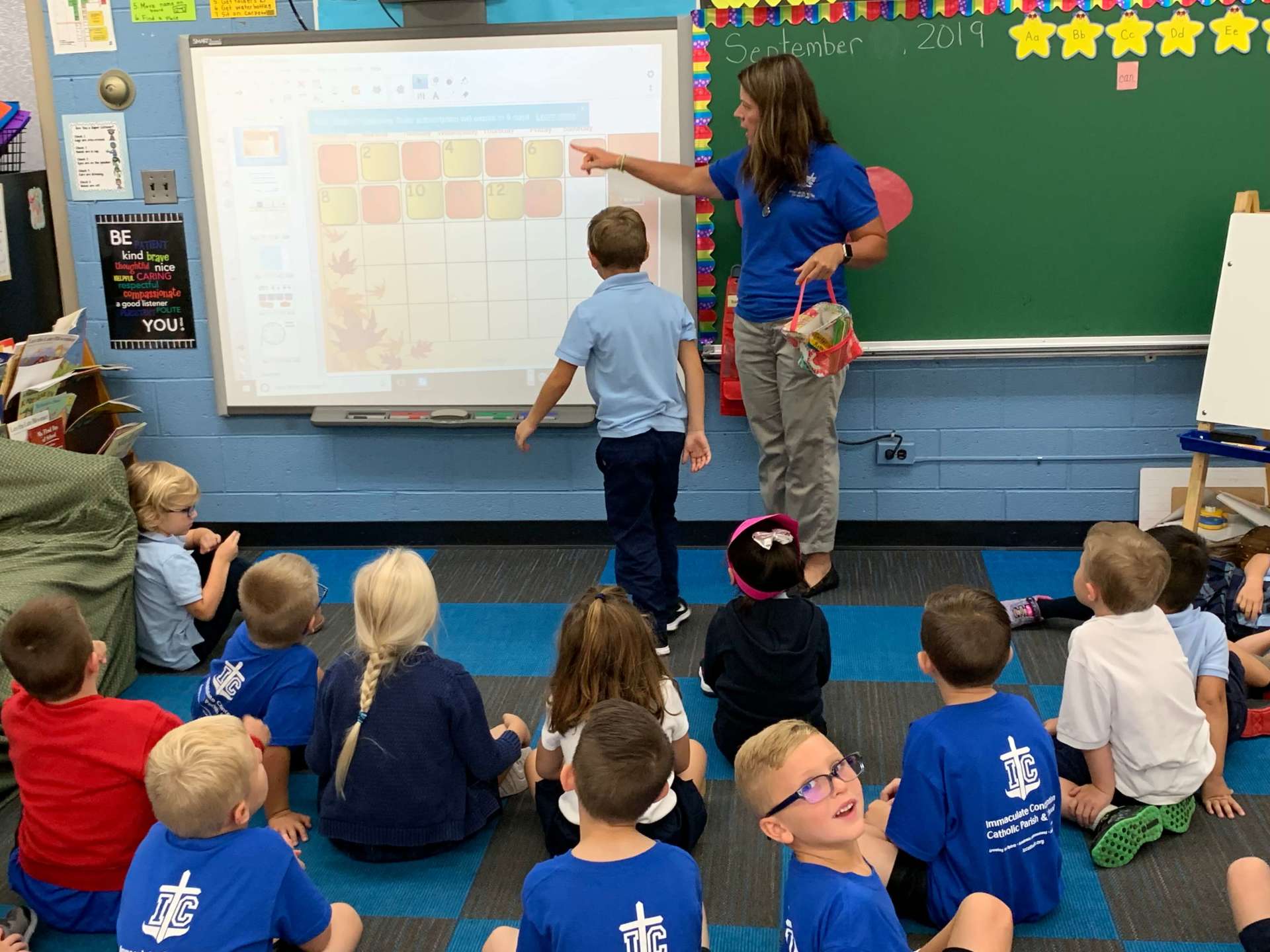 A group of children are sitting on the floor in front of a white board