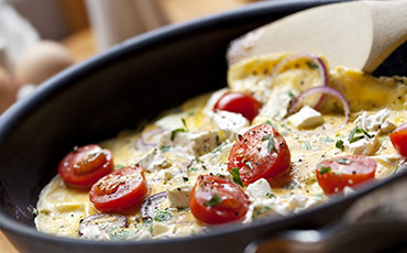Omelet in pan with cherry tomatoes, red onion, and feta cheese.