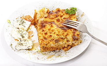 Lasagna slice on a plate with feta cheese and a fork.