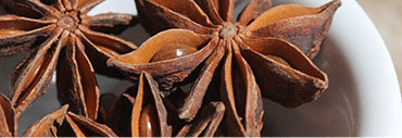 Close-up of star anise spices in a white bowl. The spices are dark brown and star-shaped.