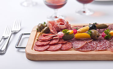 Charcuterie board with salami, olives, and pickled vegetables, served with red wine and silverware.