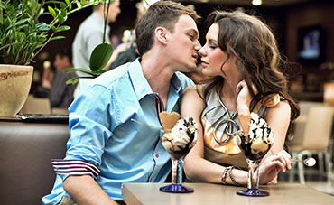 Couple kissing over ice cream in a restaurant.