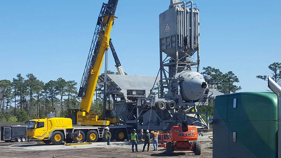 Yellow crane and truck lifting a large industrial structure at a construction site under a clear sky