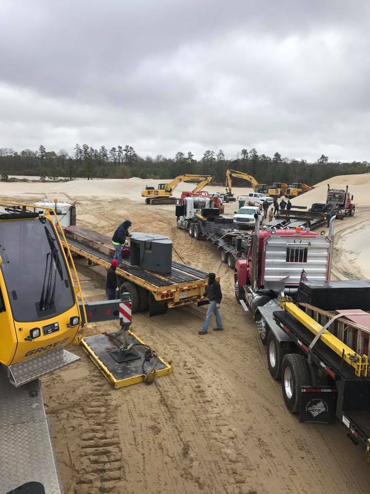 Heavy construction machines and trucks working on a muddy site under cloudy skies