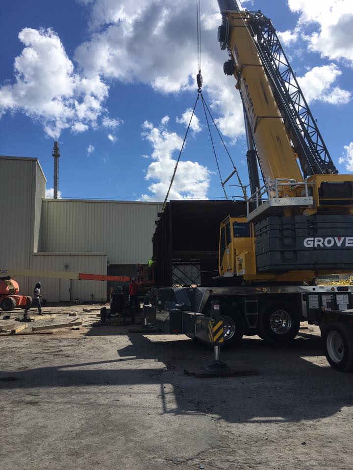 Yellow crane at an industrial site with workers and equipment under a blue sky