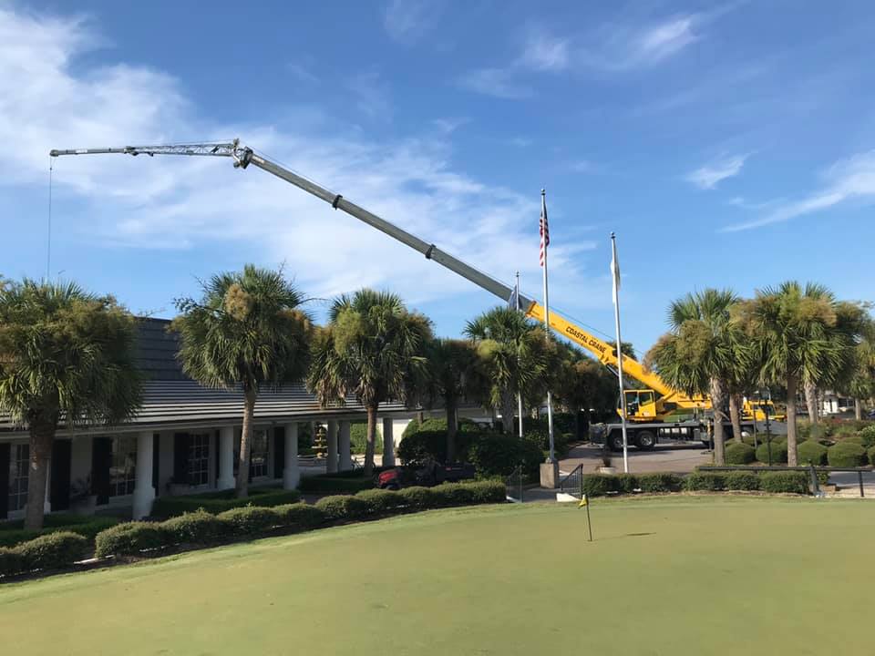 Crane lifting equipment over a golf course beside a clubhouse and palm trees
