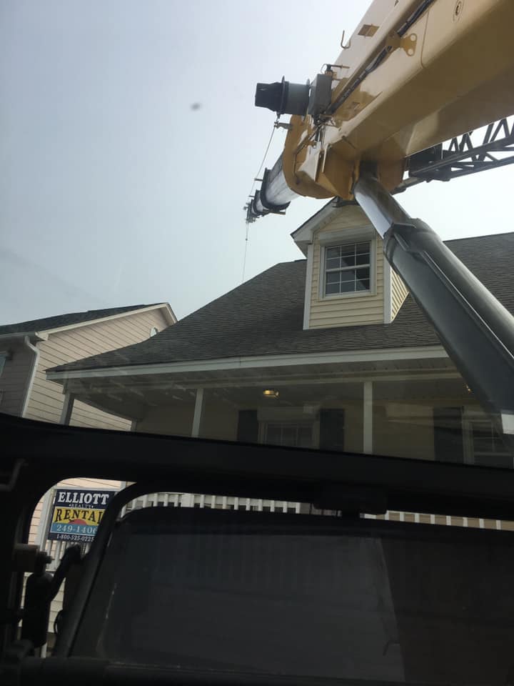 Utility truck boom reaching above a house roof in a suburban driveway