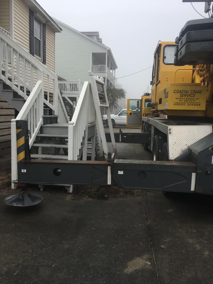 Heavy construction equipment beside a house, with white railings and a yellow machine on a wet driveway