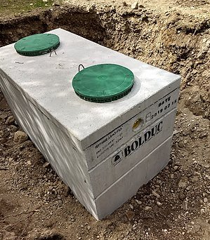 A concrete septic tank with two green lids is sitting in the dirt.