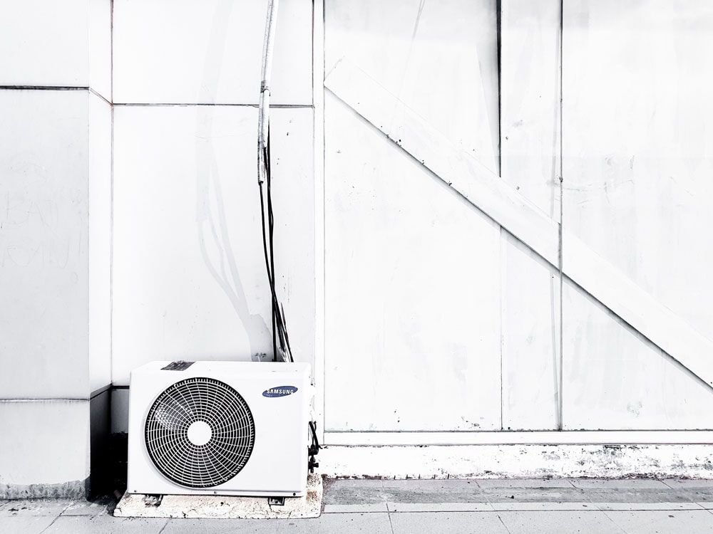 A/C Ventilation — Air Conditioner Cleaning In Cairns, QLD A White Air Conditioner is Sitting on the Side of a Building — Air-Con Cleaning Specialists in Redlynch, QLD