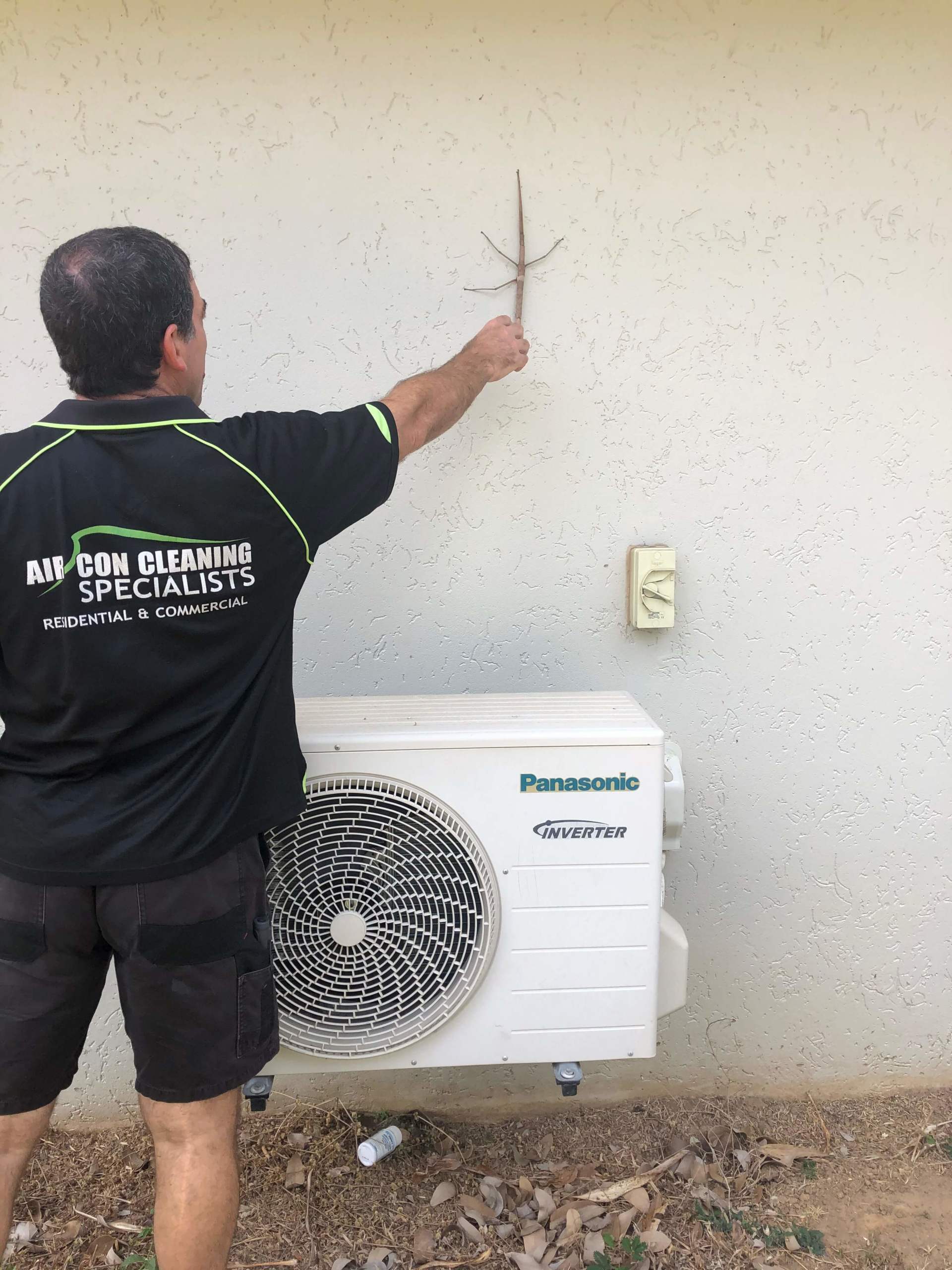 A Man in a Black Shirt is Standing Next to a Panasonic Air Conditioner — Air-Con Cleaning Specialists in Redlynch, QLD A Man in a Black Shirt is Standing Next to a Panasonic Air Conditioner — Air-Con Cleaning Specialists in Redlynch, QLD