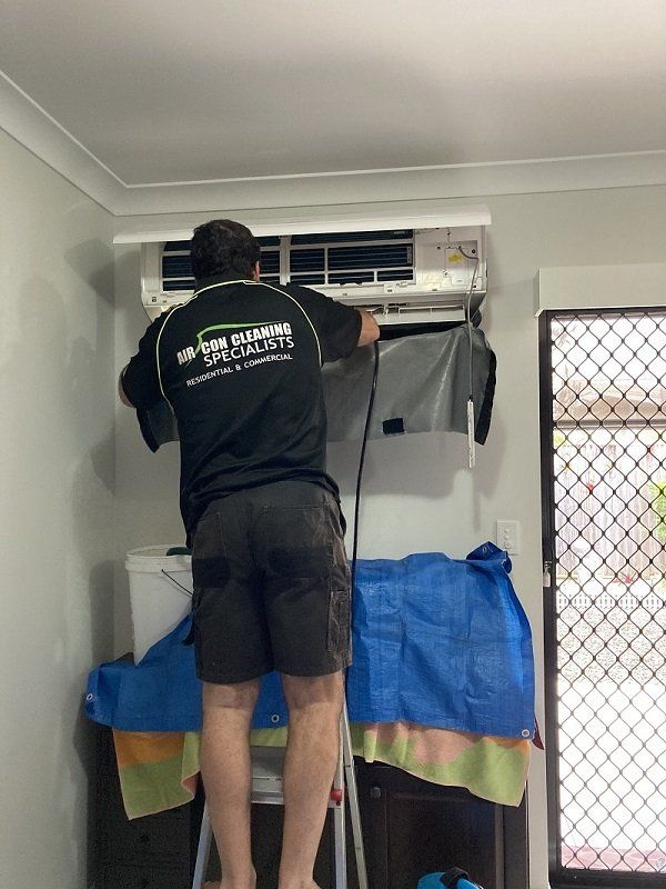 Cleaning Precautions — Air Conditioner Cleaning In Cairns, QLD A Man is Standing on a Ladder Cleaning an Air Conditioner — Air-Con Cleaning Specialists in Redlynch, QLD