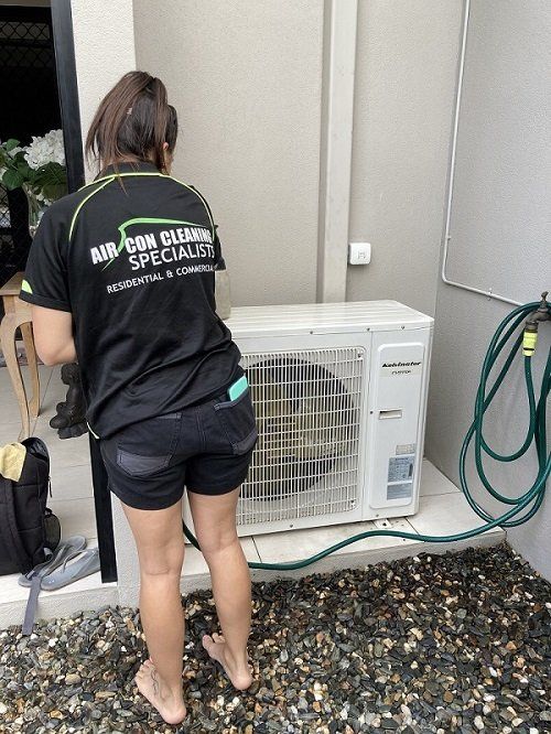 Regularly-cleaned Air Cons — Air Conditioner Cleaning In Cairns, QLD A Woman is Standing Next to an Air Conditioner With a Hose Attached to It — Air-Con Cleaning Specialists in Redlynch, QLD