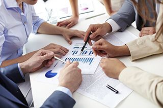 business people around a table pointing at graphs on a document