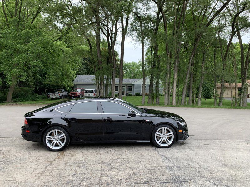 A black car is parked in a parking lot with trees in the background.