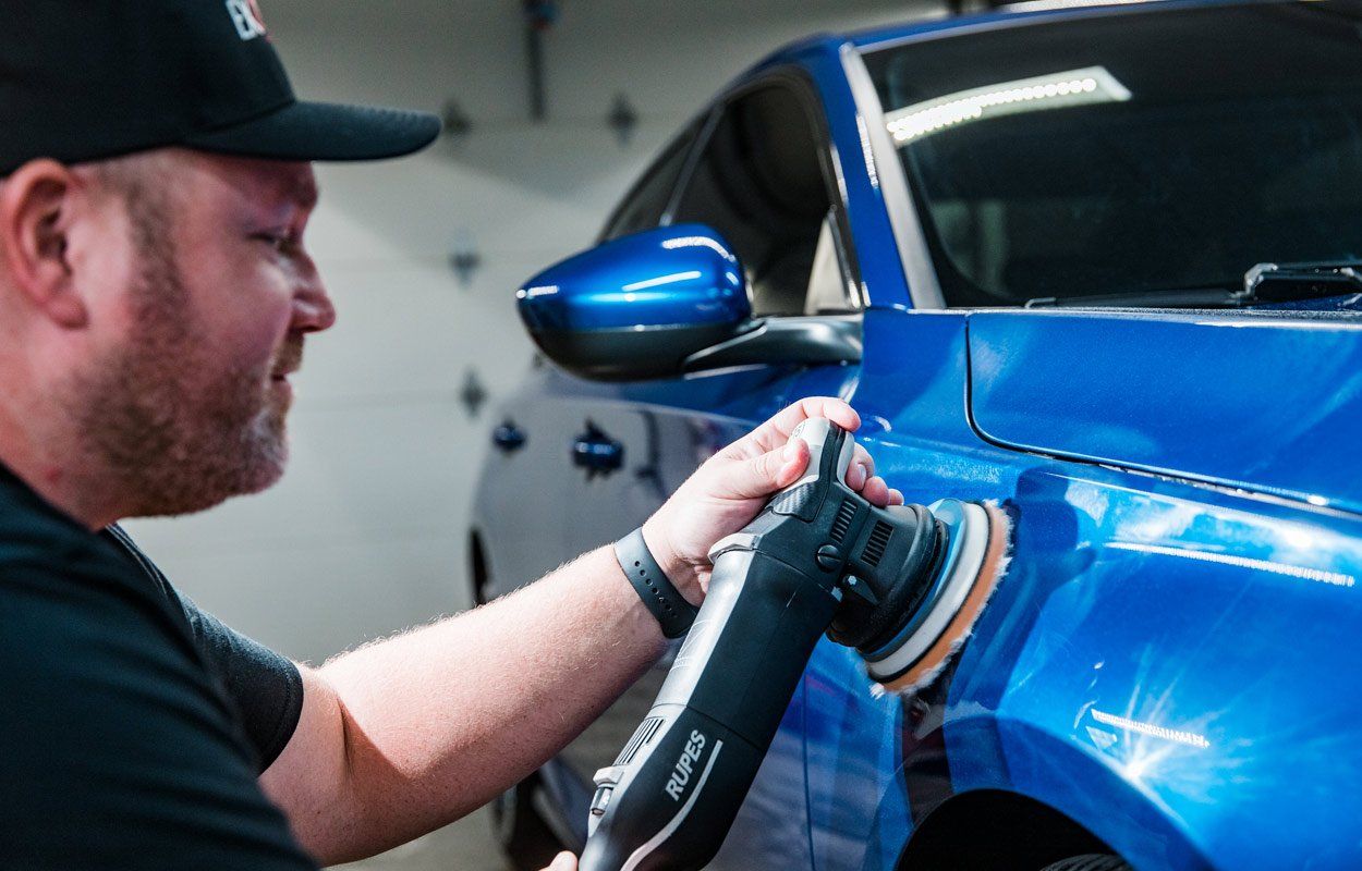 A man is polishing a blue car with a machine.