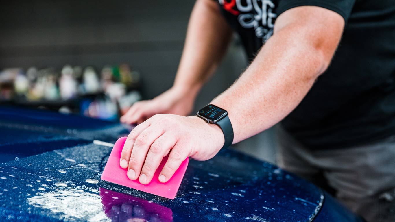 A man is cleaning a blue car with a pink sponge.