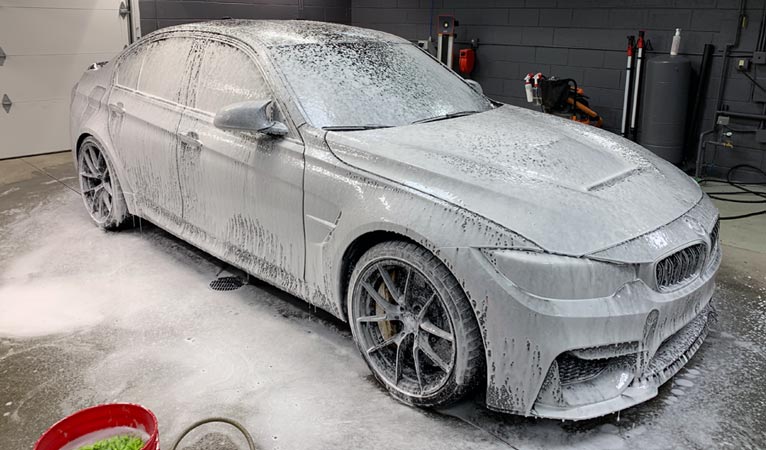 A bmw m3 is covered in foam in a garage.