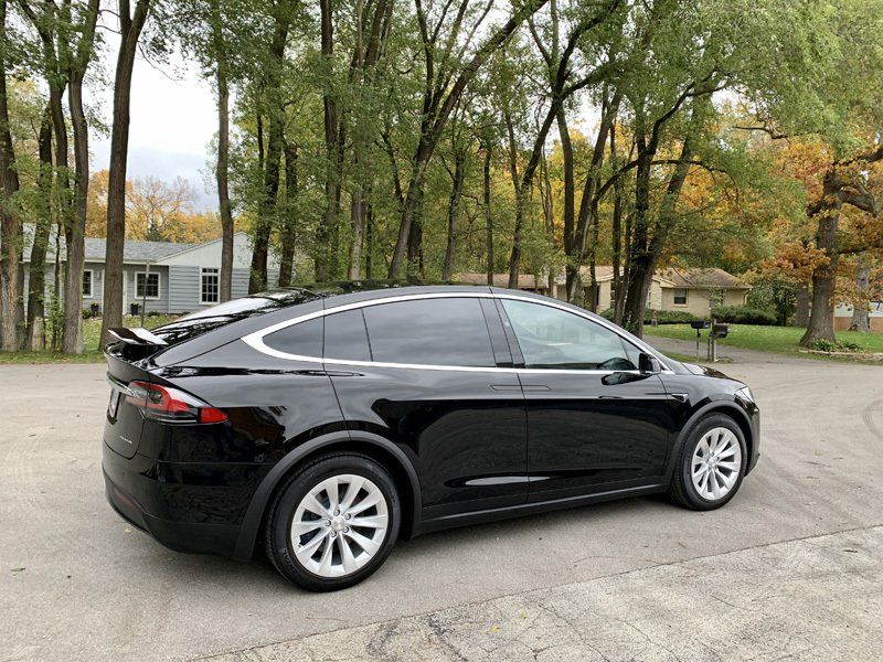 A black tesla model x is parked in a driveway next to trees.